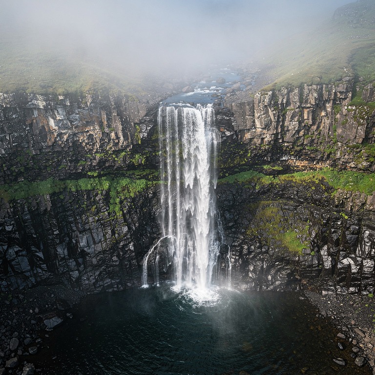 A gentle waterfall cascades down a rocky cliff, creating a m... | ShopAyahuascaRetreats