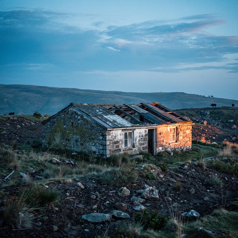 A solitary, worn stone cottage on a barren hillside, evoking... | ShopAyahuascaRetreats